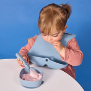 Child eating berry yogurt from a blue bowl and spoon set against a blue background