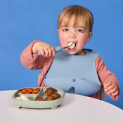 Child eating with a blue bib against a blue background