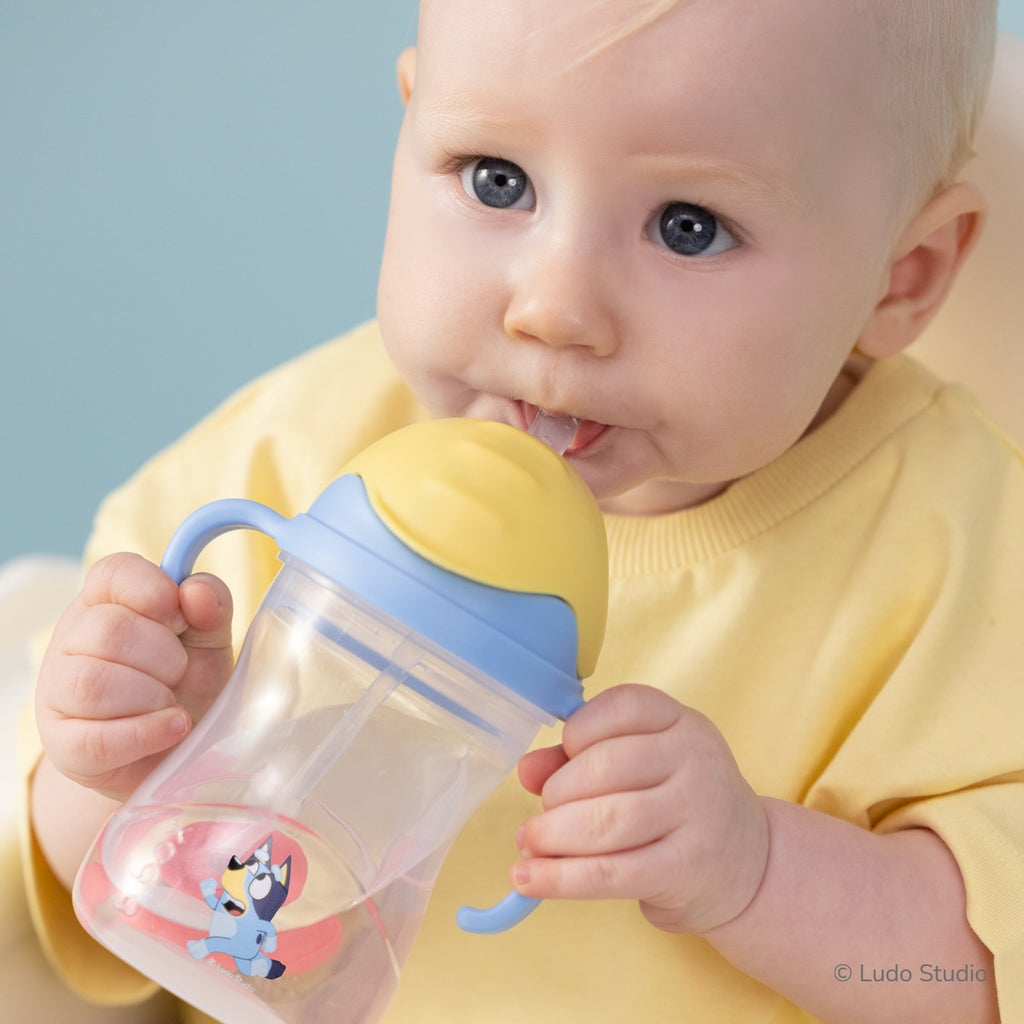 Baby holding a sippy cup with Bluey character on a light blue background