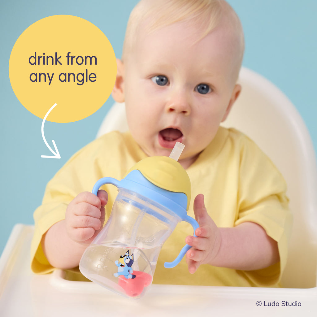 Baby holding a Bluey sippy cup with a blue handle against a light blue background.