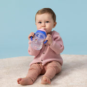 Baby in a pink outfit holding a blue sippy cup against a light blue background